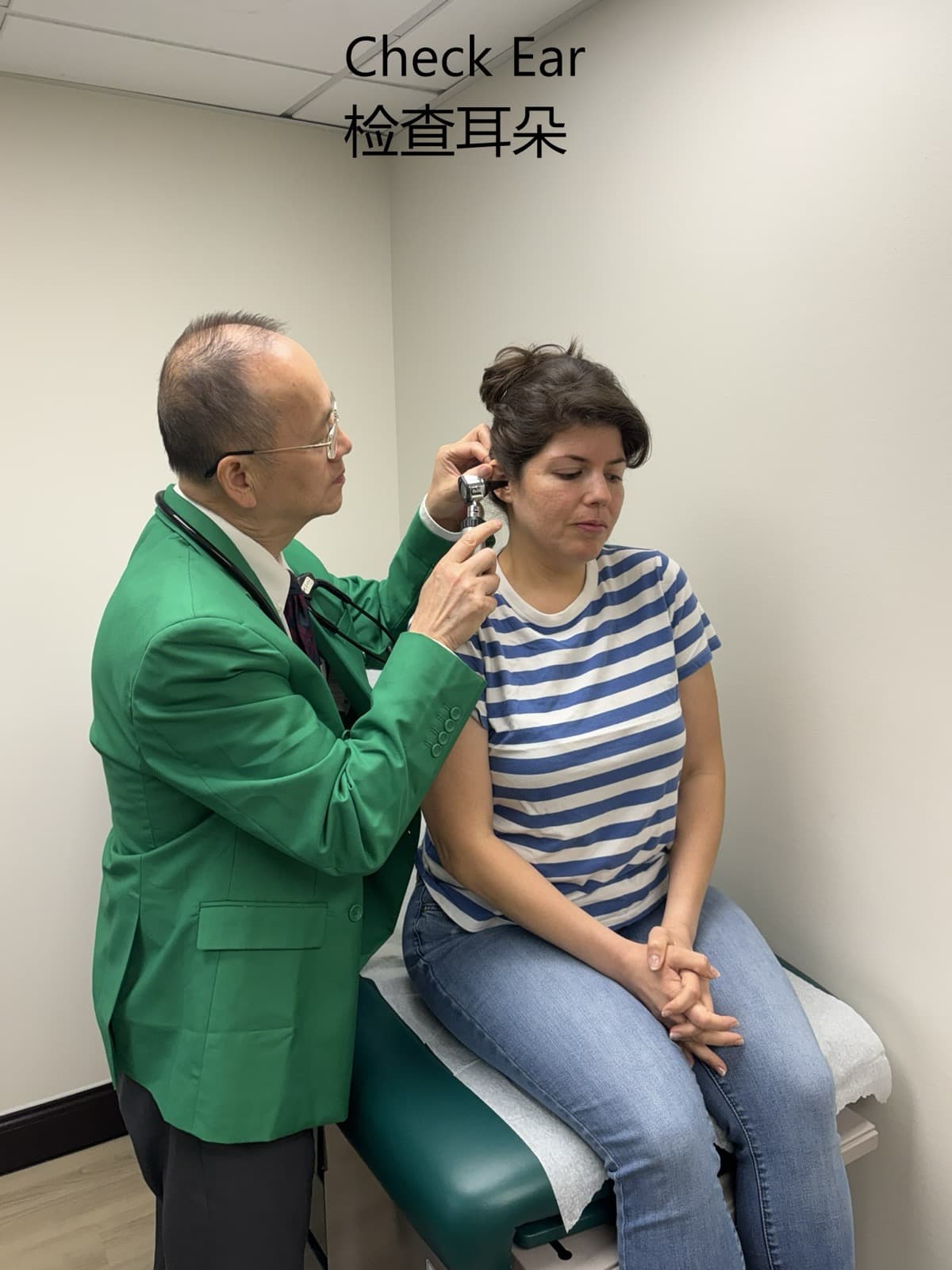 Dr. Lee in a green suit examining a female patient’s ear with an otoscope during a routine exam